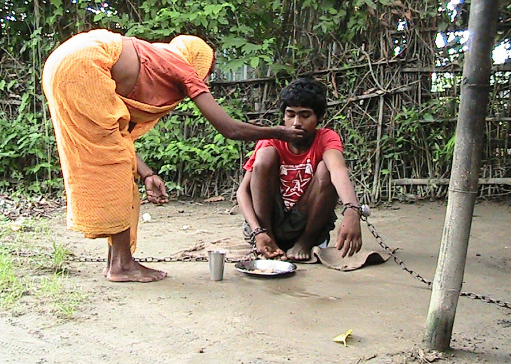 आठ वर्ष देखि साङलोमा बाँधीएका सुनसरी औरावनी गाविस ९ का अमित साहलाई बिस्कुट खुवाउँदै आमा तितरी साह । आर्थिक अभावका कारण साहको उचार हुन सकेको छैन । तस्बिरः अजितकुमार झा, इनरुवा(रासस)